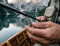 Angler inspecting guides on a fishing rod by a calm lake.