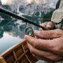 Angler inspecting guides on a fishing rod by a calm lake.
